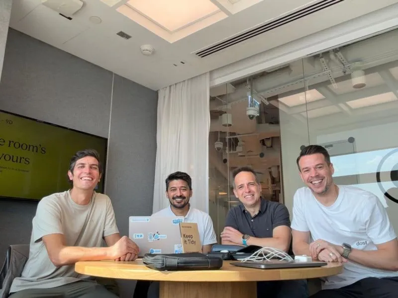The Dost team around a meeting-room table, laptops out