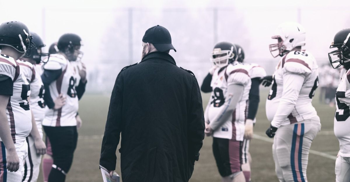 An American football coach standing among his players on the field