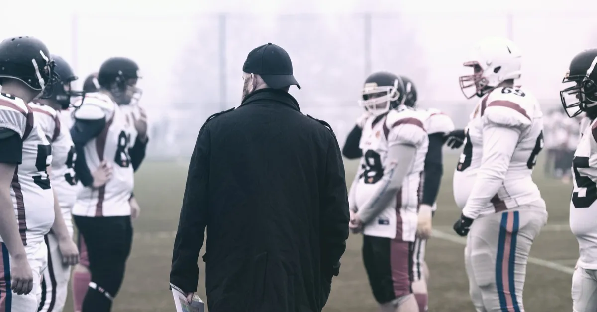 An American football coach standing among his players on the field
