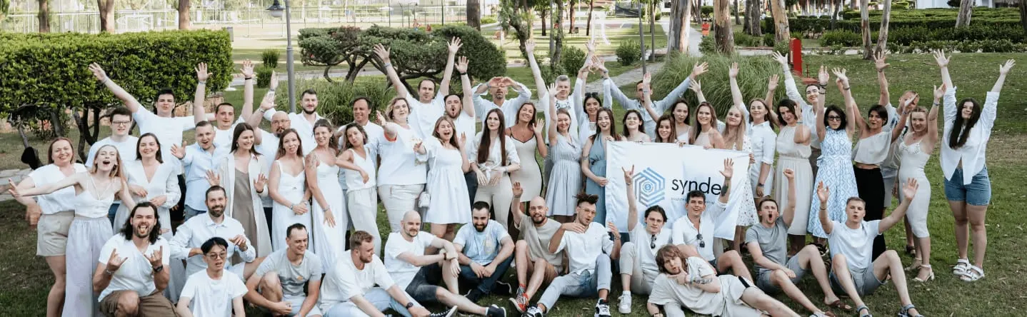 About sixty Synder staff in white on a lawn, arms raised